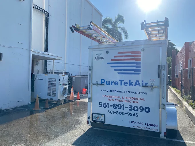 Pure Tek Air enclosed trailer with a roof-mounted ladder rack beside a commercial building