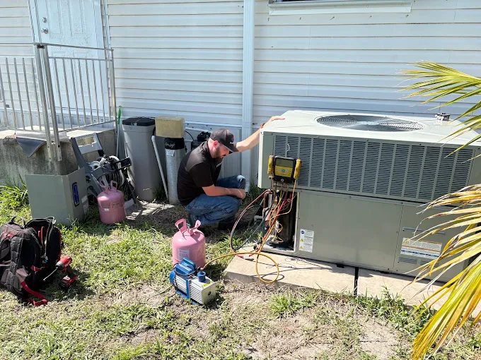 Technician checking an outdoor condenser with a digital manifold gauge set and refrigerant cylinders