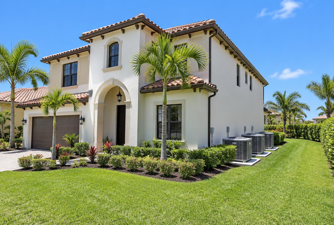 Newly built two-story Mediterranean-style Wellington, Florida home with cream stucco walls, barrel tile roof and three new AC condensers on raised pads along the side wall, young palms and manicured lawn